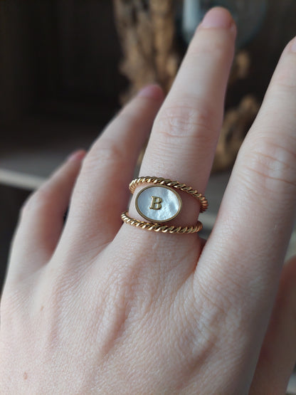 bijou personnalisable; bague en acier inoxydable doré avec un effet torsadé et un ovale nacré et une initiale au centre