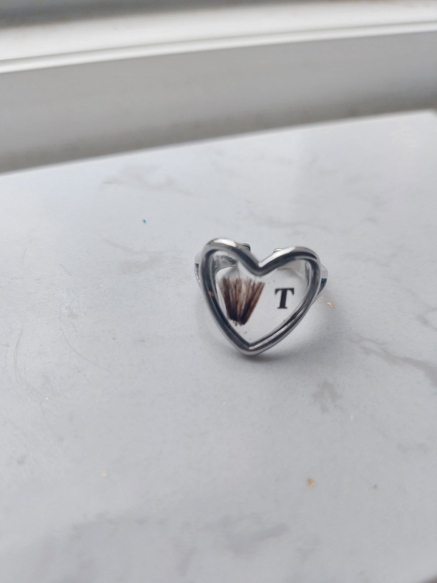 bijoux souvenir: bague en forme de coeur en acier inoxydable argenté avec insertion de cheveux dans le fond de la bague et une initiale