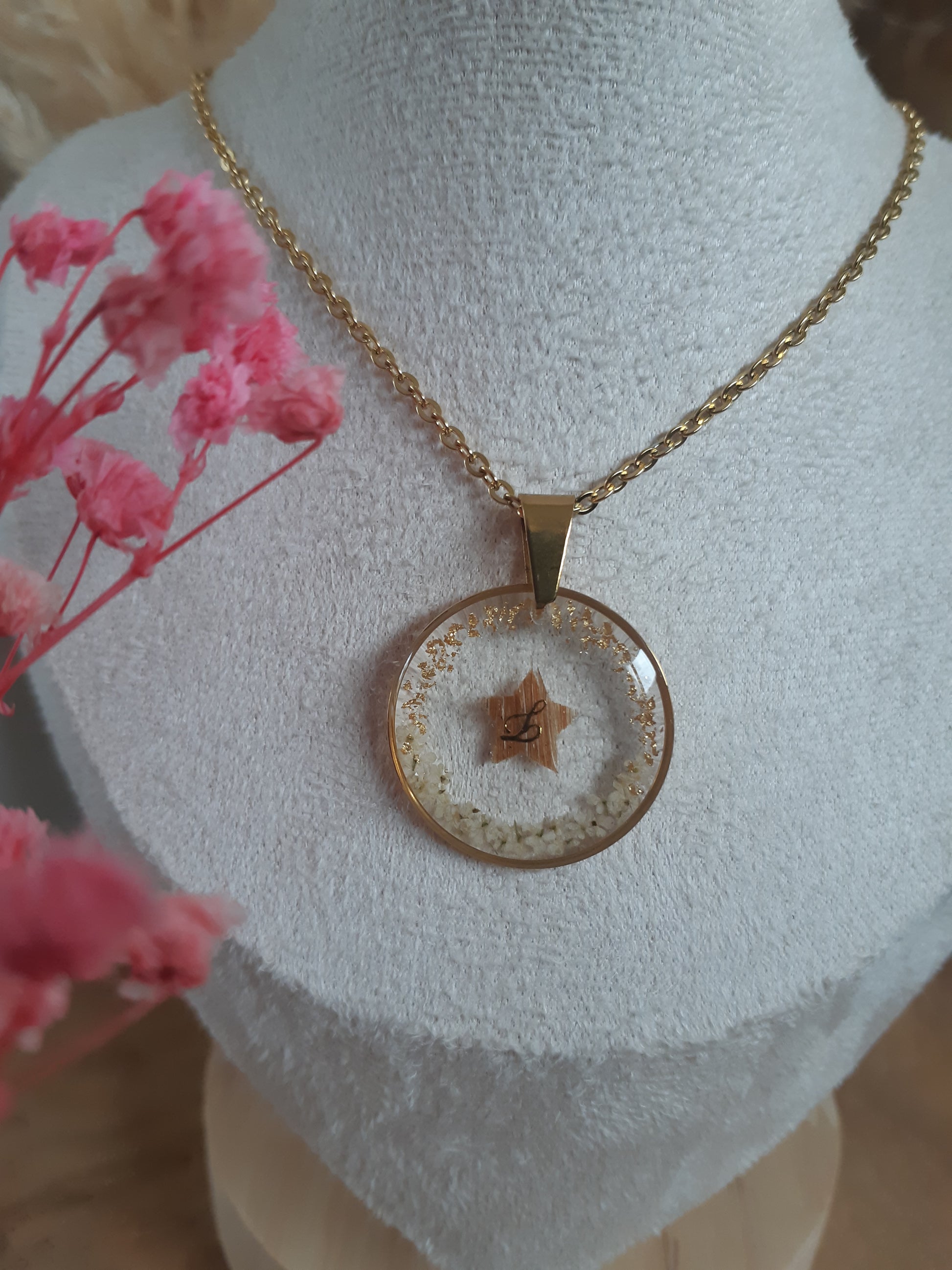 collier souvenir en acier inoxydable doré, le pendentif contient une étoile réaliser avec une mèche de cheveux, il y a des fleurs blanche et des feuilles d'or