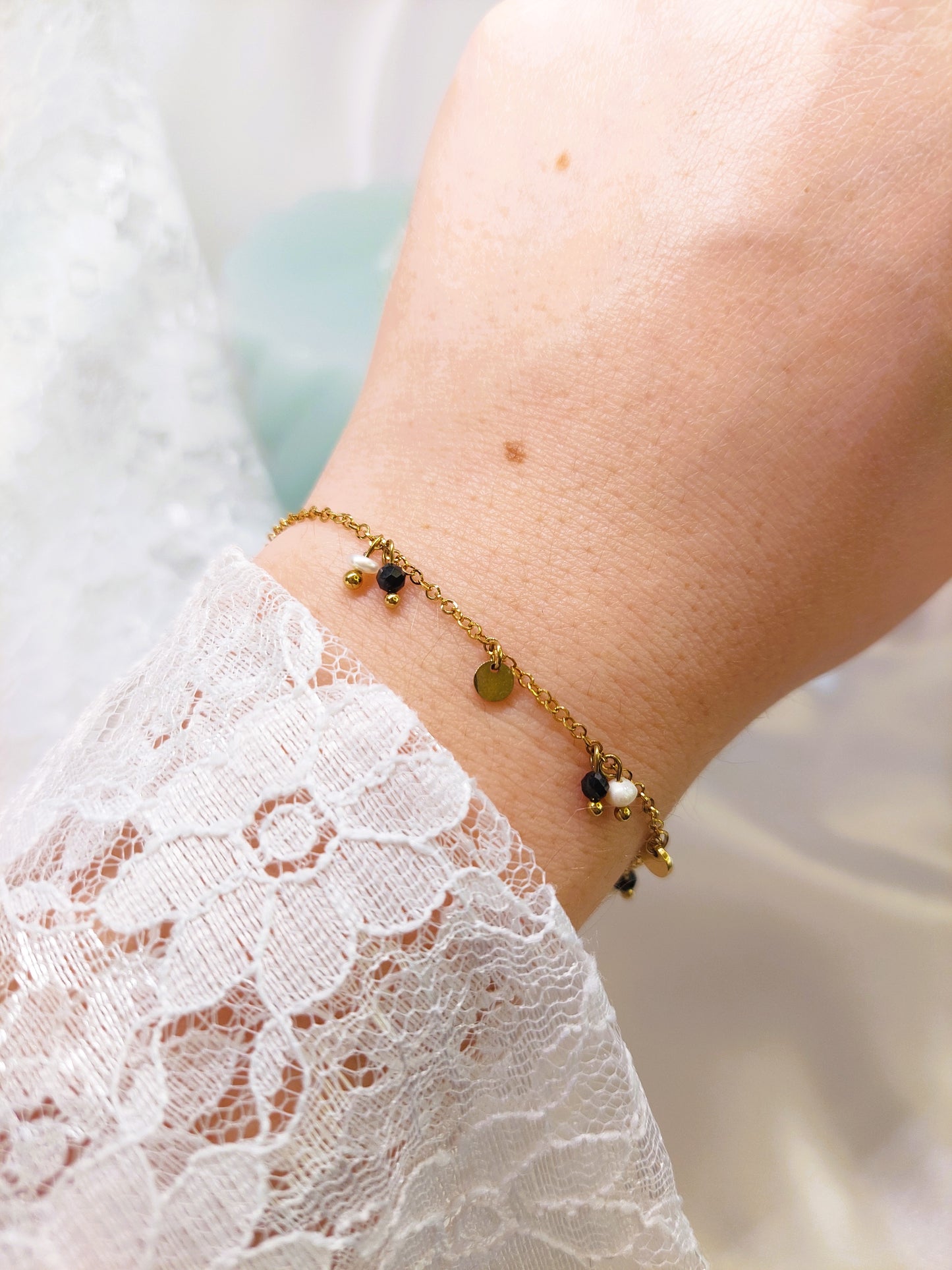 bracelet doré avec des petite pampilles et des petite perles blanche et noire