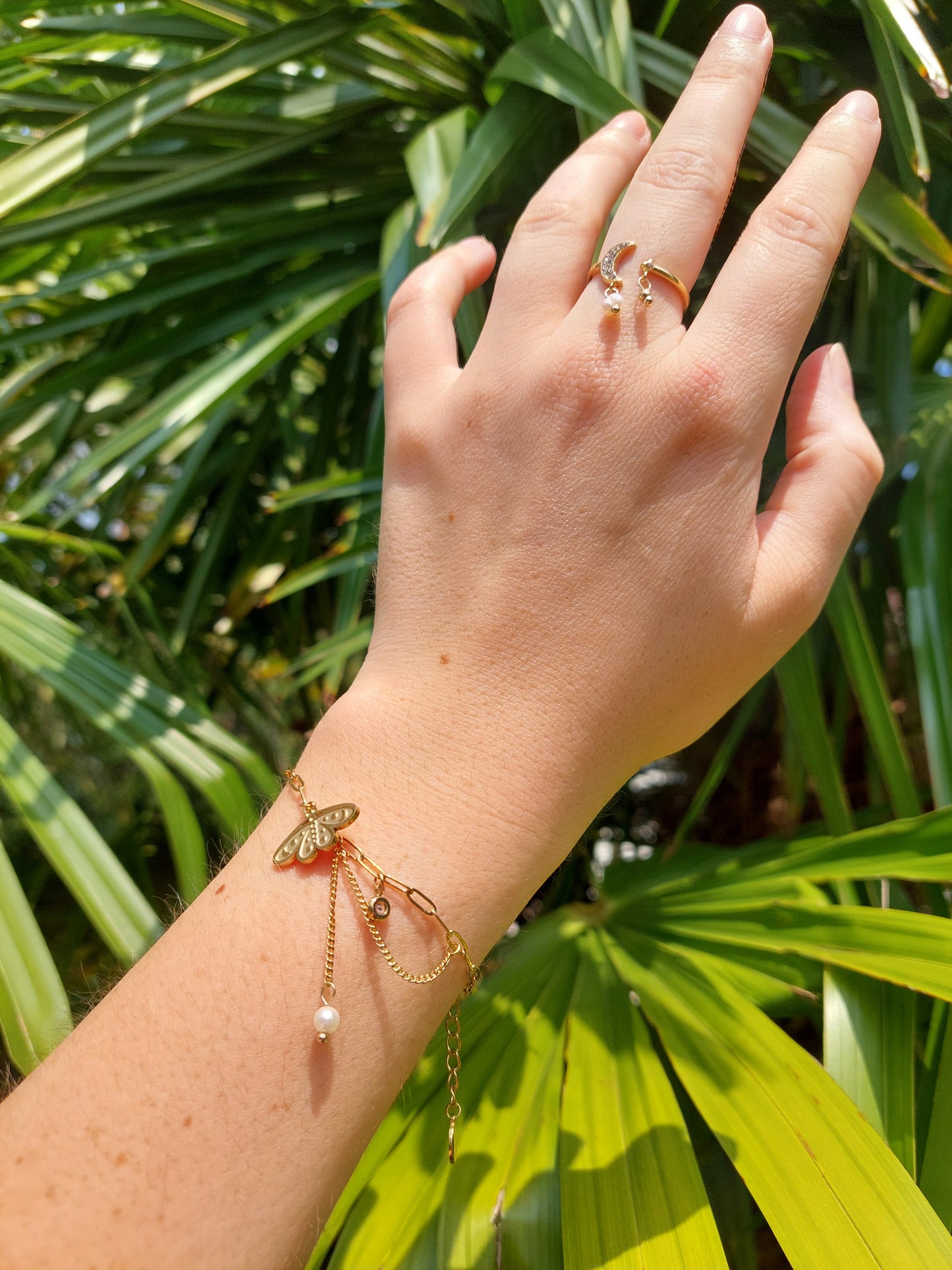 Bracelet breloque avec un charme papillon de nuit et un strass et une chainette à la qu'elle est suspendu une perle blanche