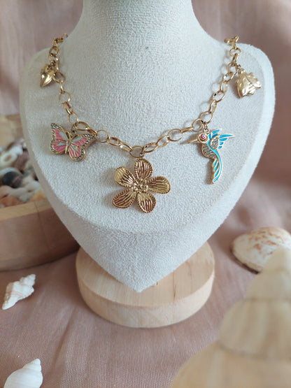 collier en acier inoxydable doré en grosse mailles et plusieurs charme. une fleurs central doré puis un oiseau blau, un papillon rose et une coccinelle et un coeur doré