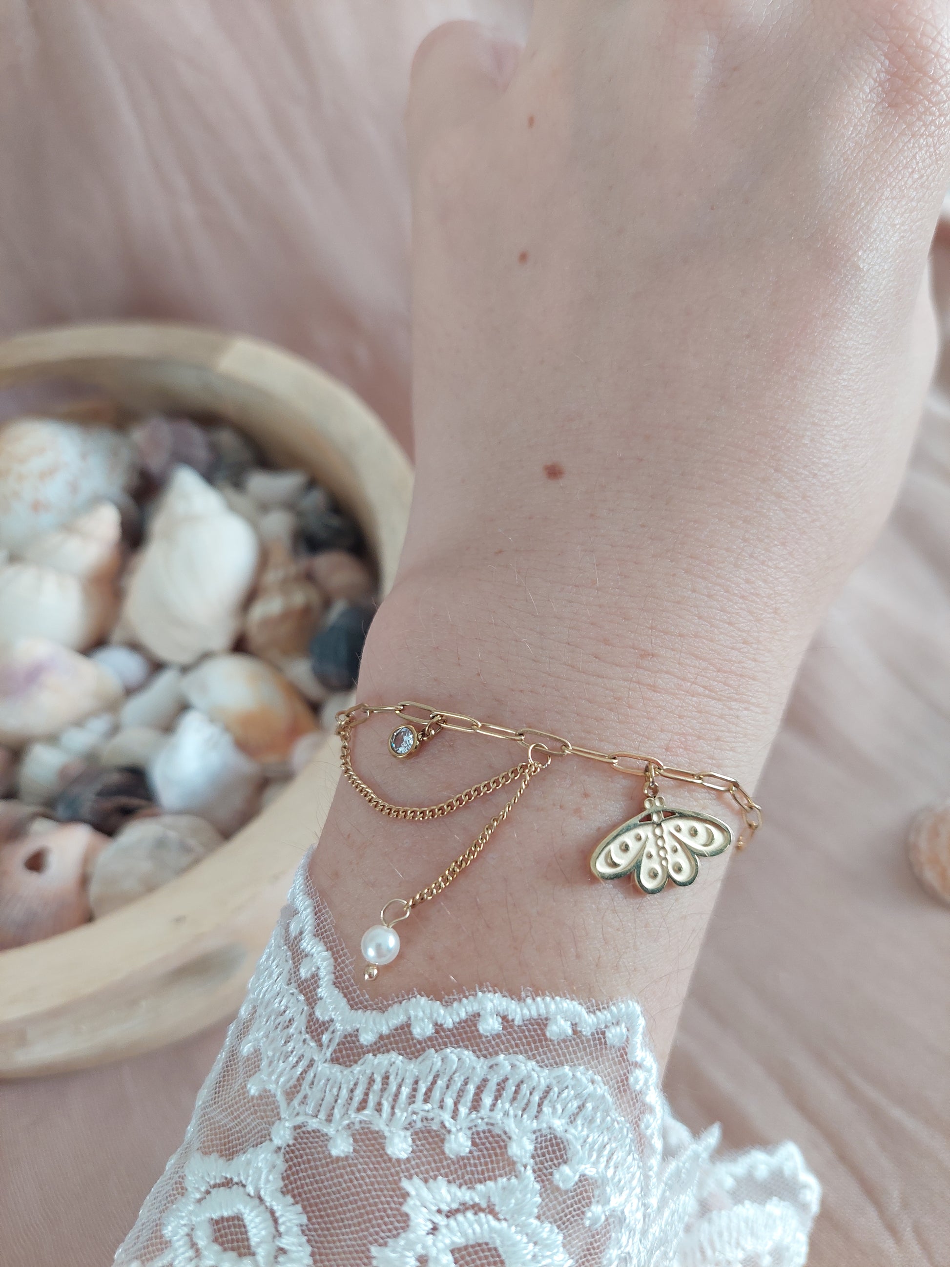 Bracelet breloque avec un charme papillon de nuit et un strass et une chainette à la qu'elle est suspendu une perle blanche