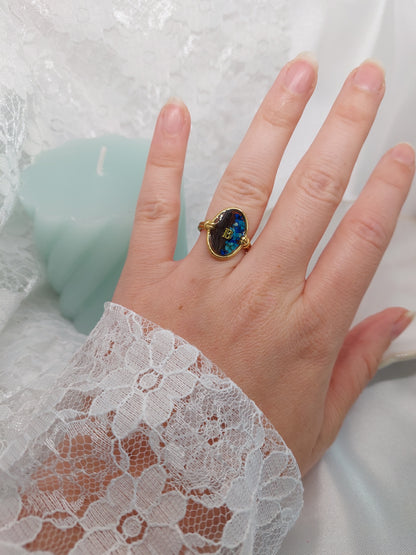 bijou souvenir, bague réglable de forme ovale avec insertion de cheveux et des fleurs bleus avec une initiale au centre