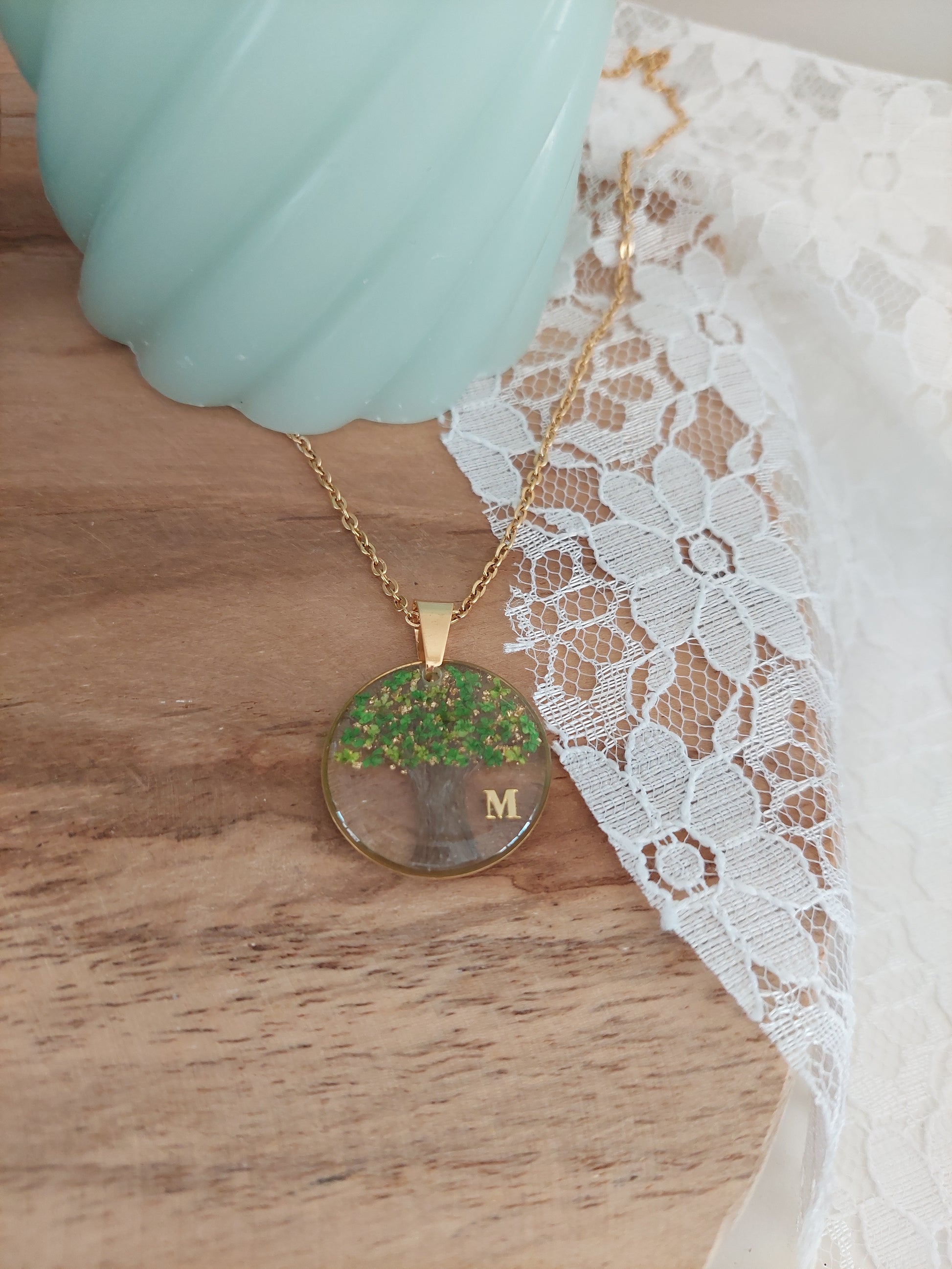 bijou souvenir avec un pendentif rond et des cheveux à l'intérieur en forme  d'arbre de vie et des fleurs séchées verte et une initiale