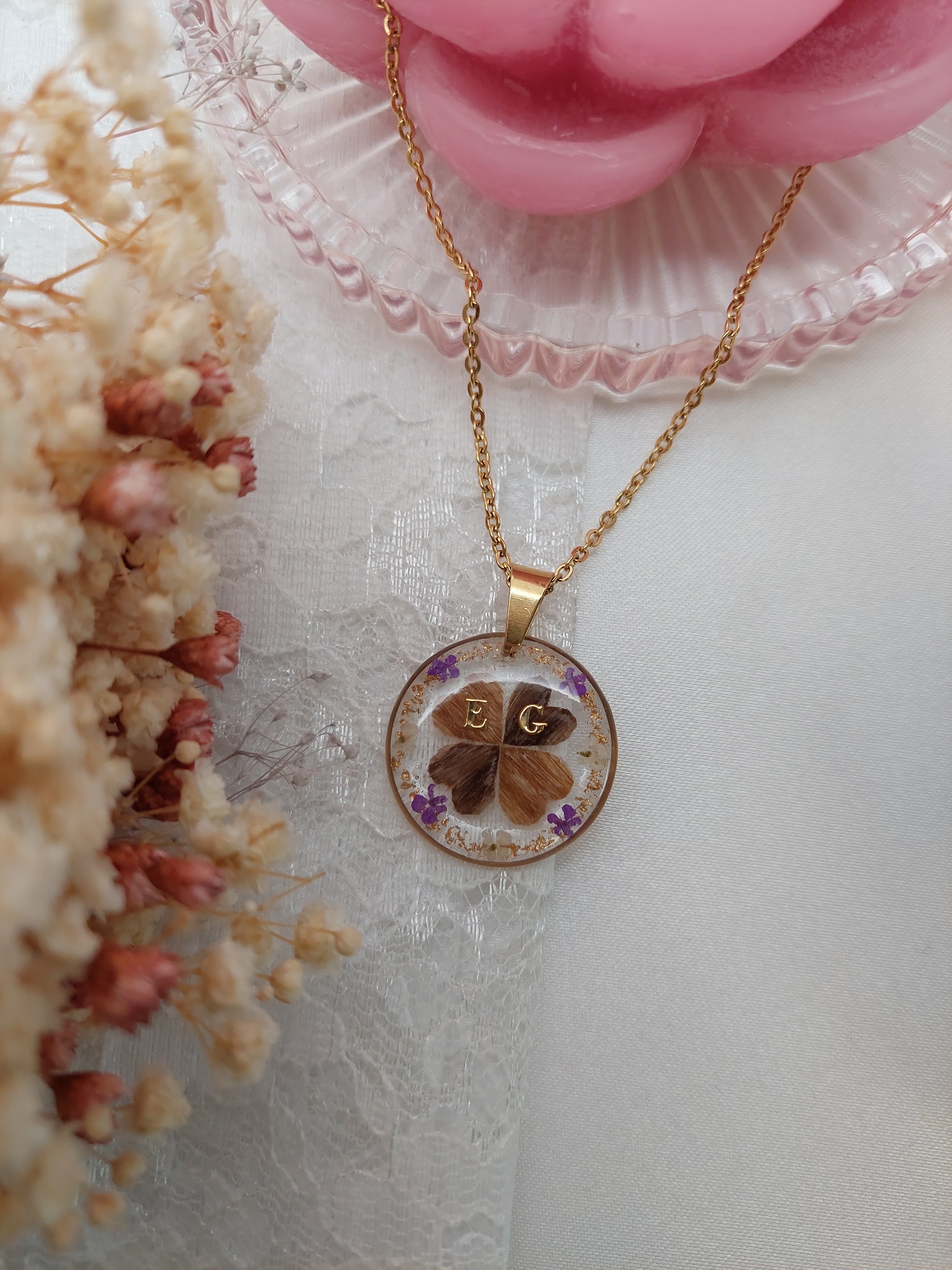 collier souvenirs avec deux mèches de cheveux différentes en forme de trèfles à quatre feuilles, avec 2 initiales et des fleurs violettes et blanches